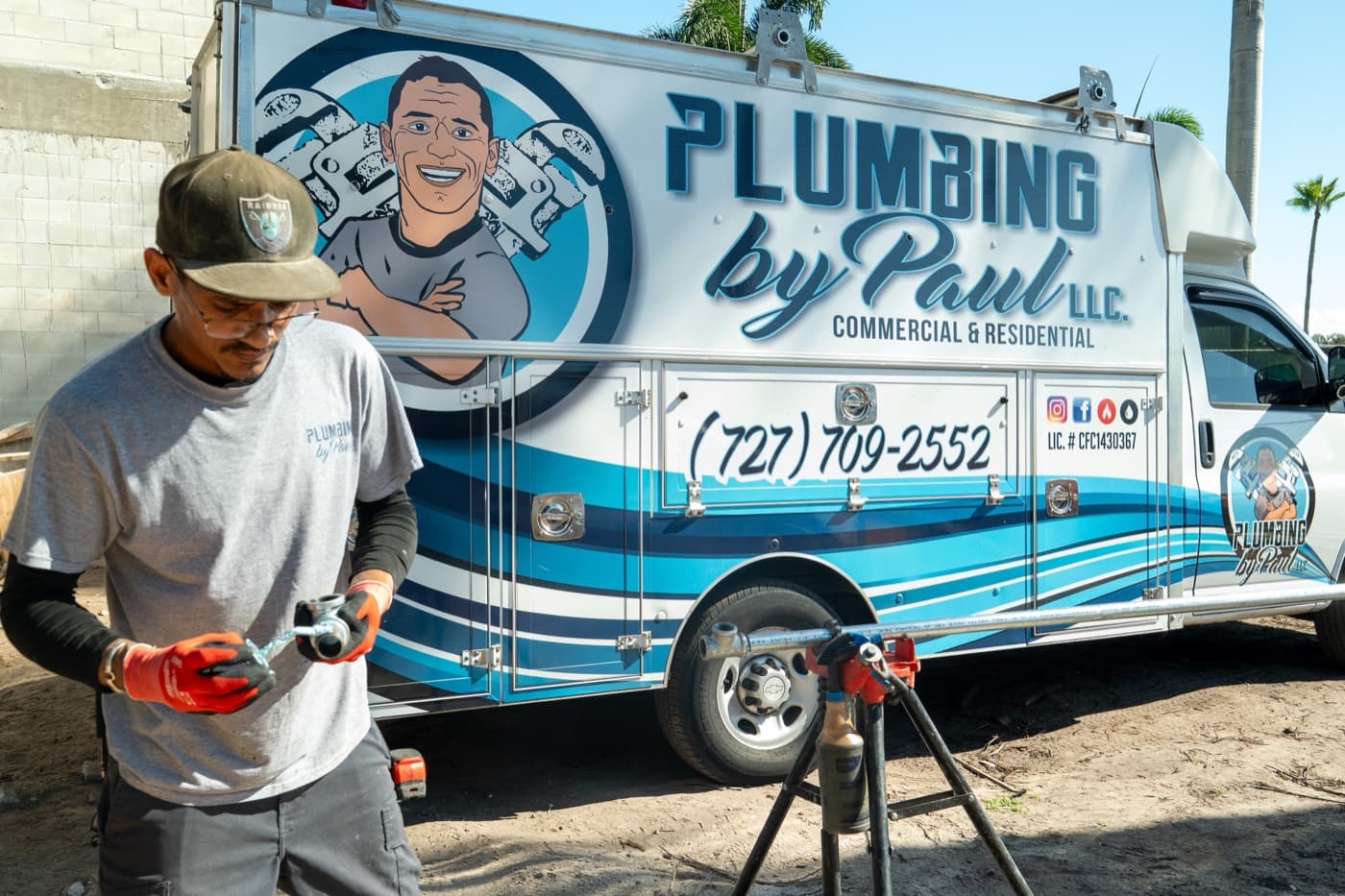 Plumber threading pipe beside a branded box truck with a 727 phone number on a Pinellas County job site