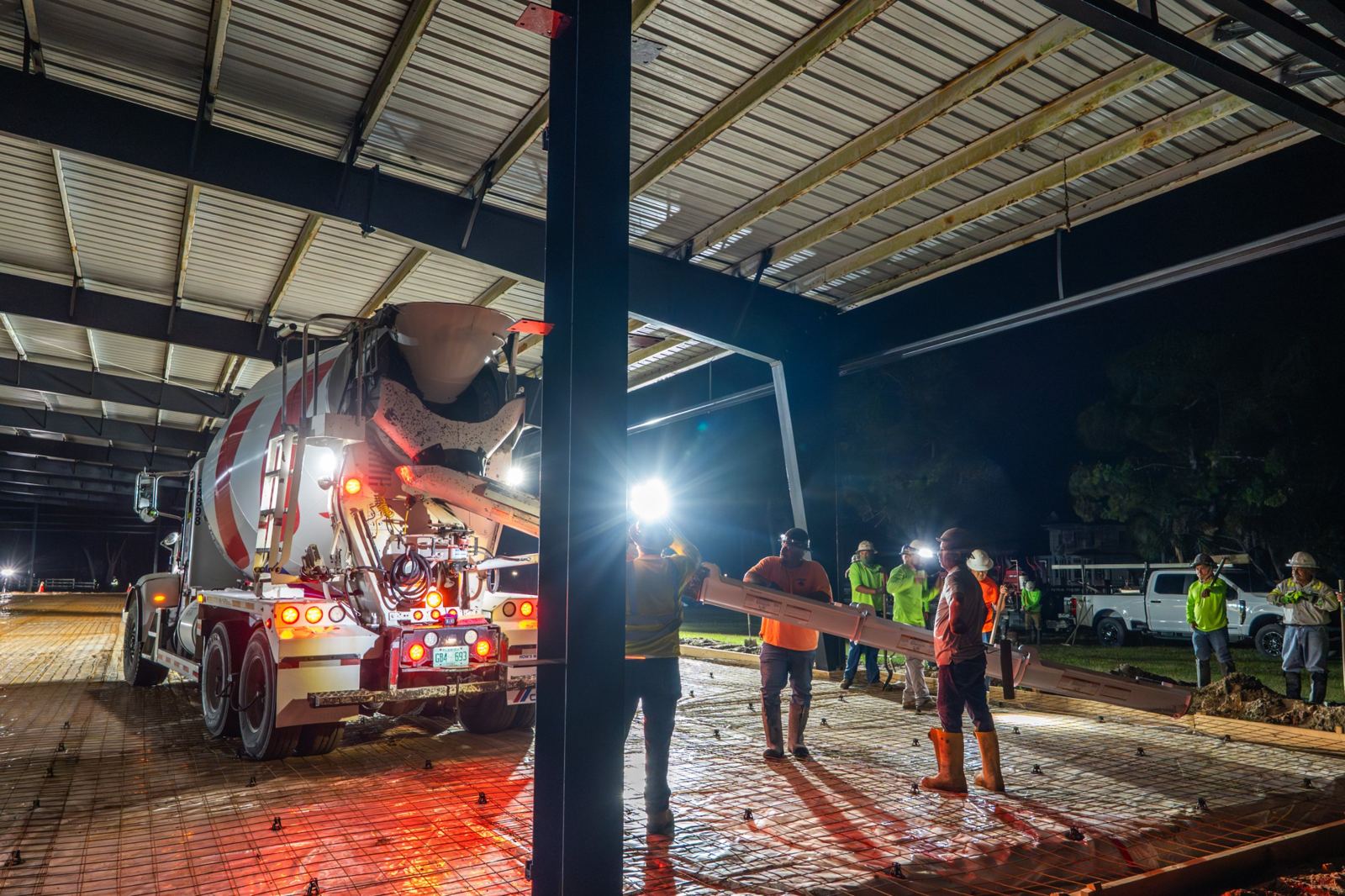 Crew guiding a concrete truck chute during a night slab pour under a steel frame