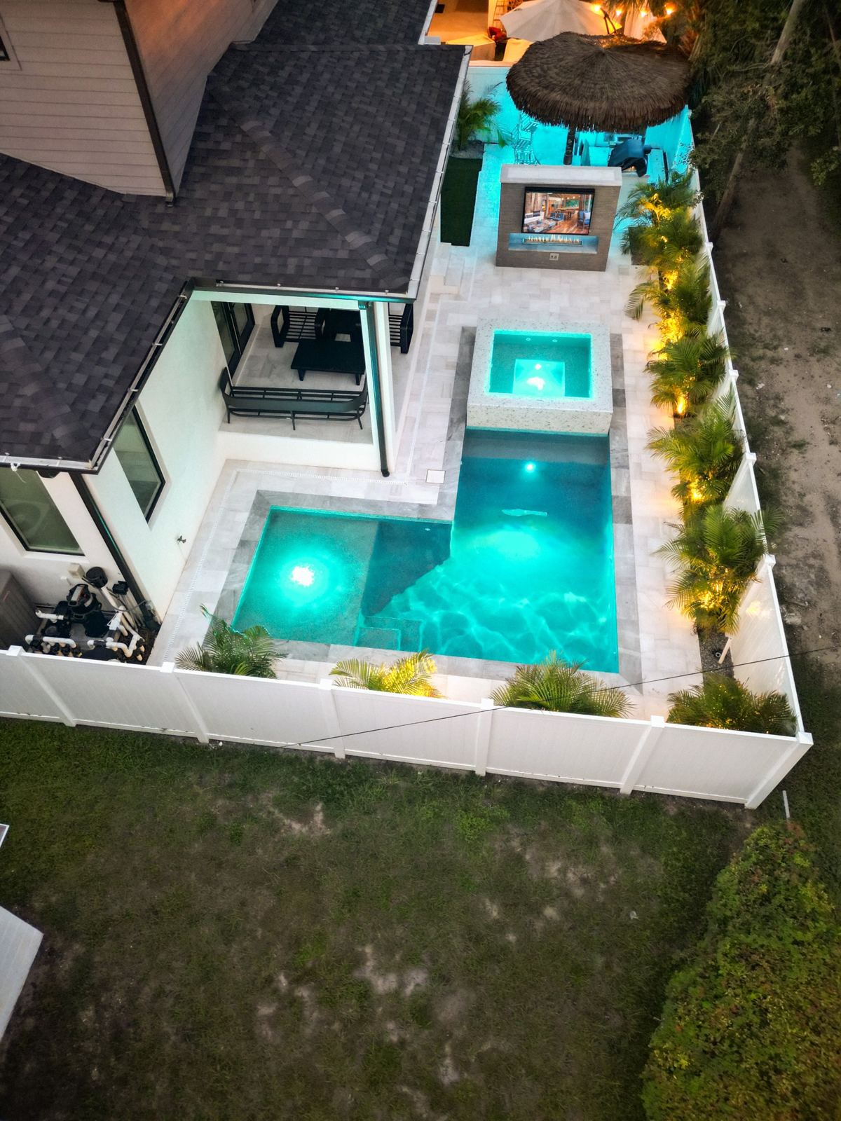 Drone view of a backyard pool, spa and outdoor fireplace lit at night