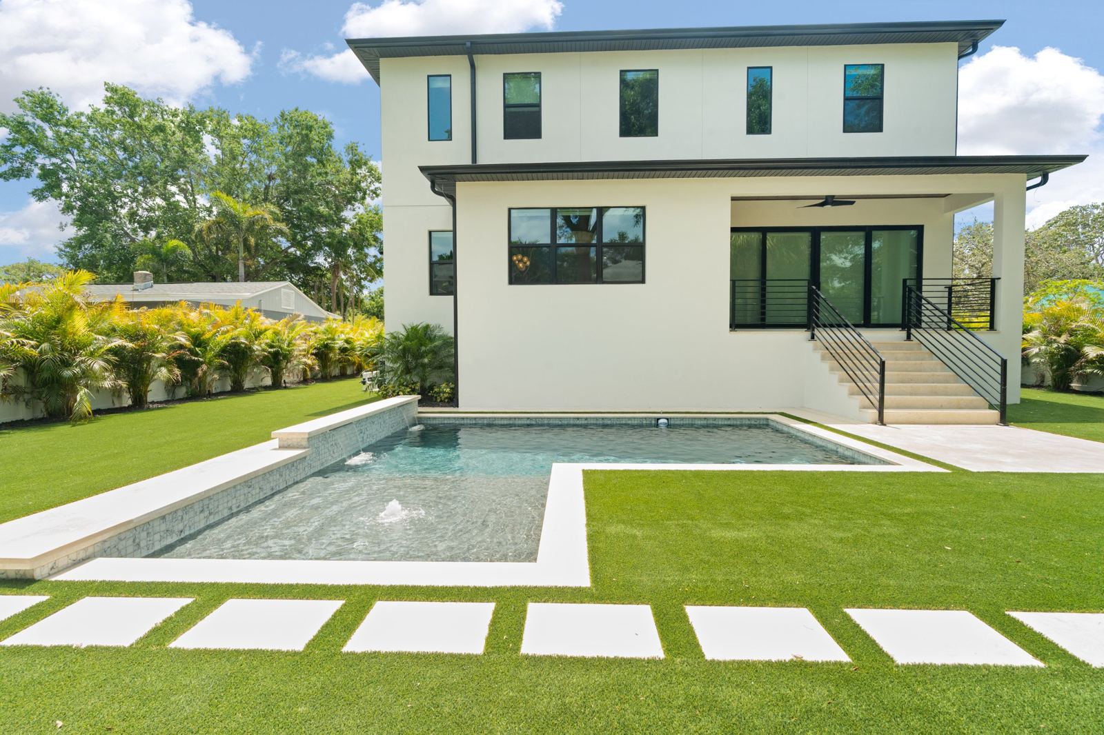 Modern new-build home with a rectangular pool, sun shelf and artificial turf