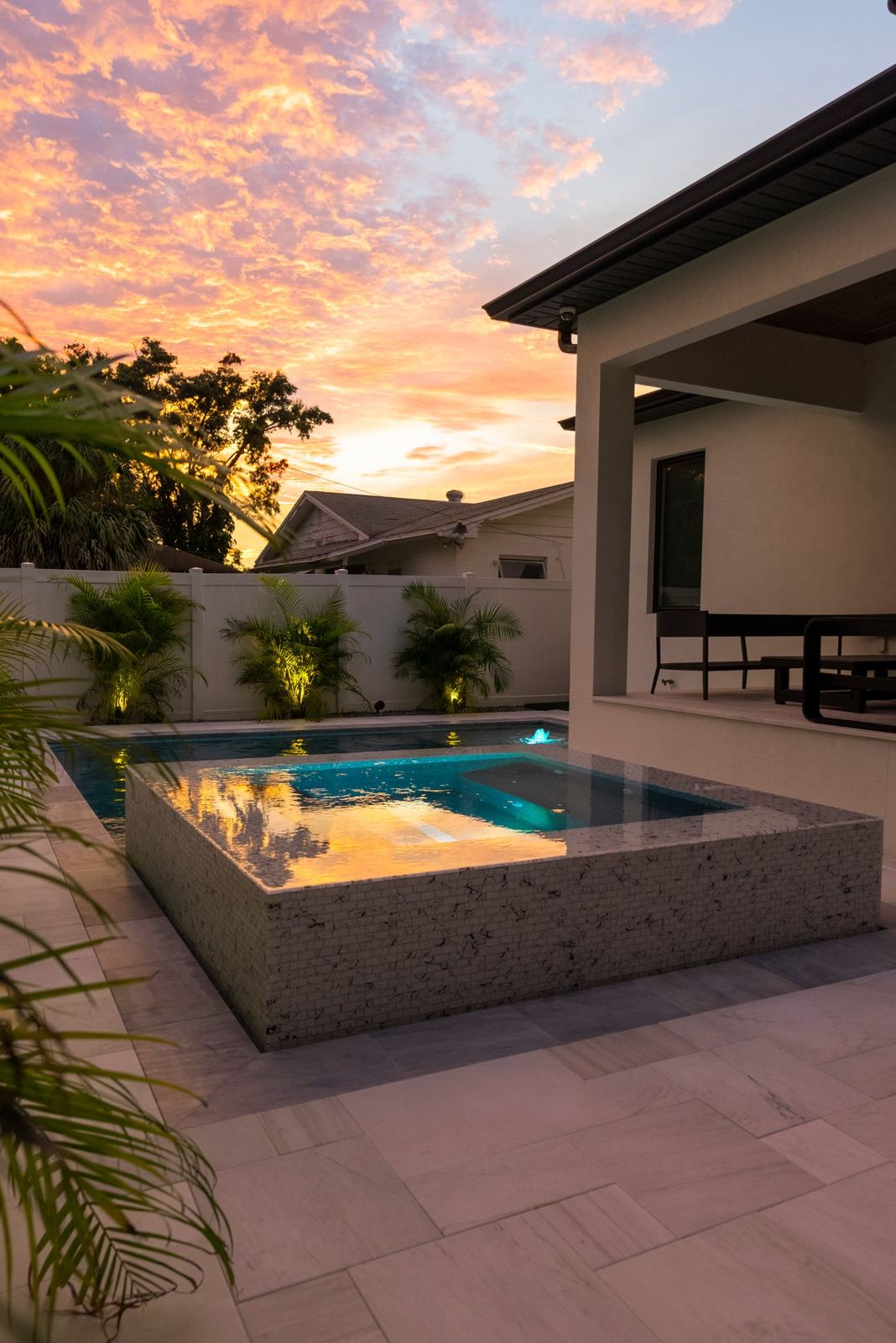 Raised spa spilling into the pool at sunset with lit palms
