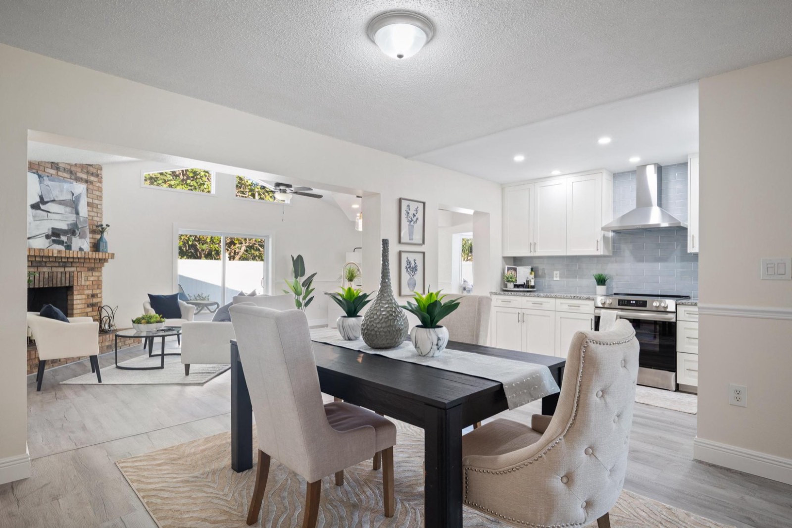 Staged open-plan dining room with a dark wood table, shot through to a white shaker kitchen and a living room with a brick fireplace