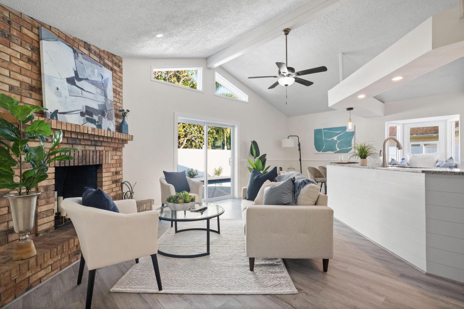 Living room with a floor-to-ceiling brick fireplace and vaulted beamed ceiling, sliding doors opening to a pool deck