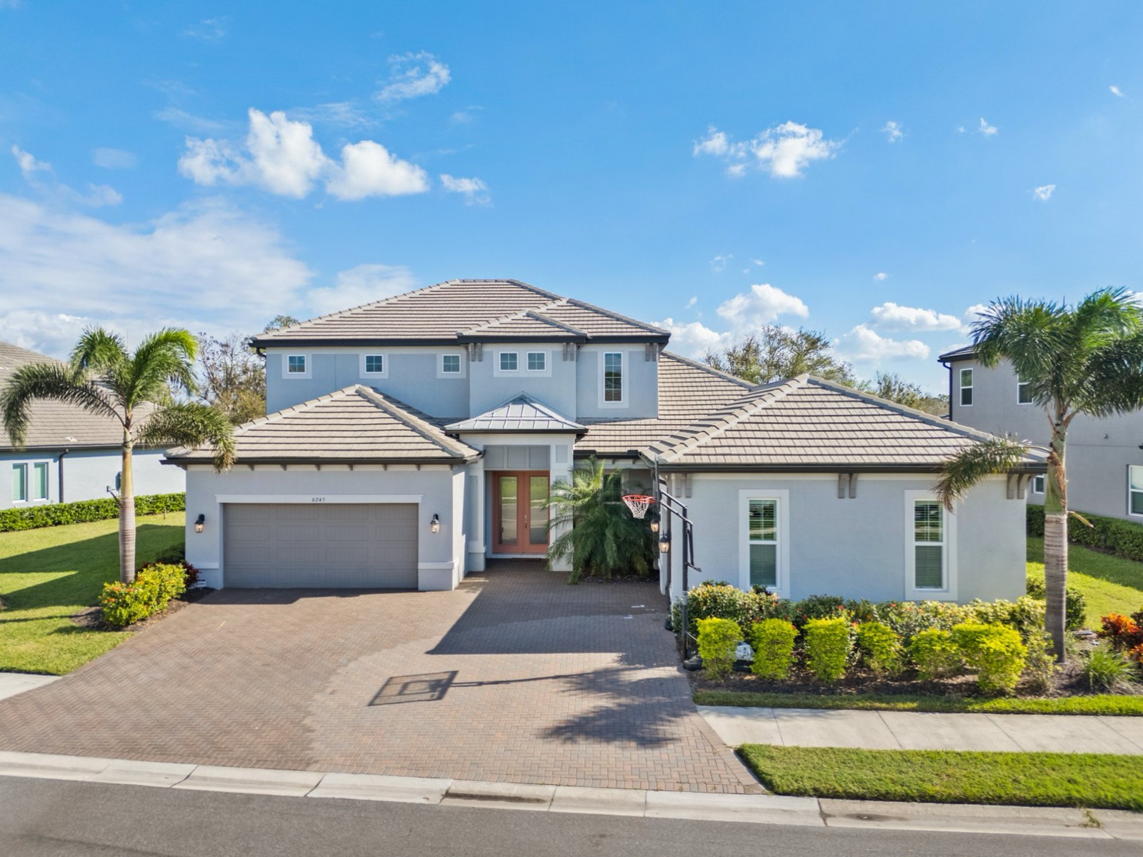 Front elevation of a two-storey Florida home with a tile roof, paver driveway and palms, photographed from an elevated angle in daylight