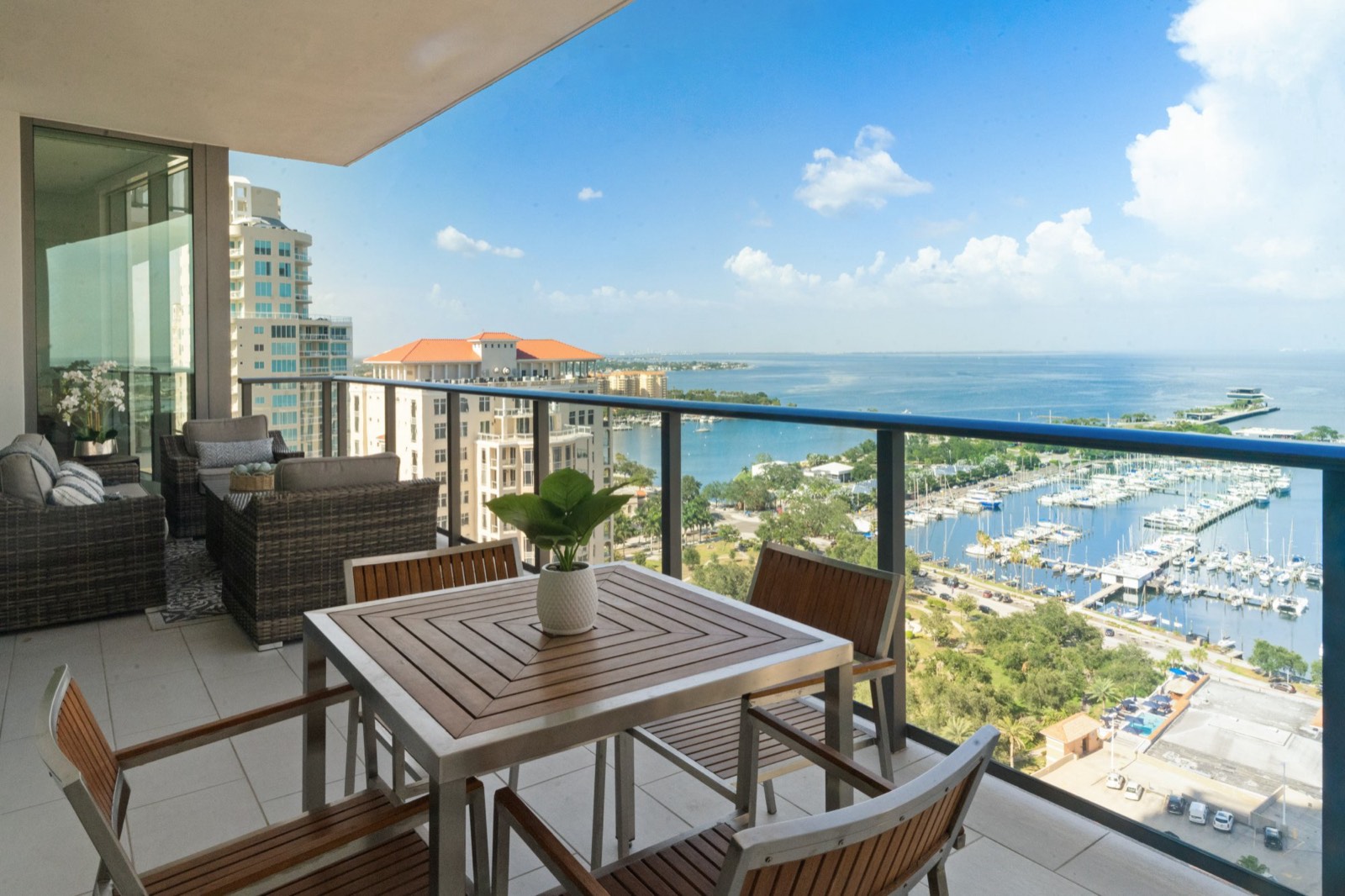 High-rise condo balcony with a dining set, overlooking a marina full of sailboats and open bay water beyond