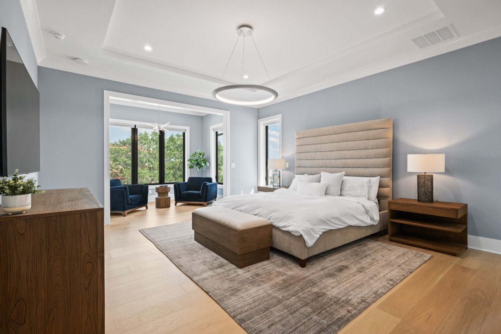 Primary bedroom with a tray ceiling, upholstered headboard and a ring pendant, opening into an adjoining sitting room