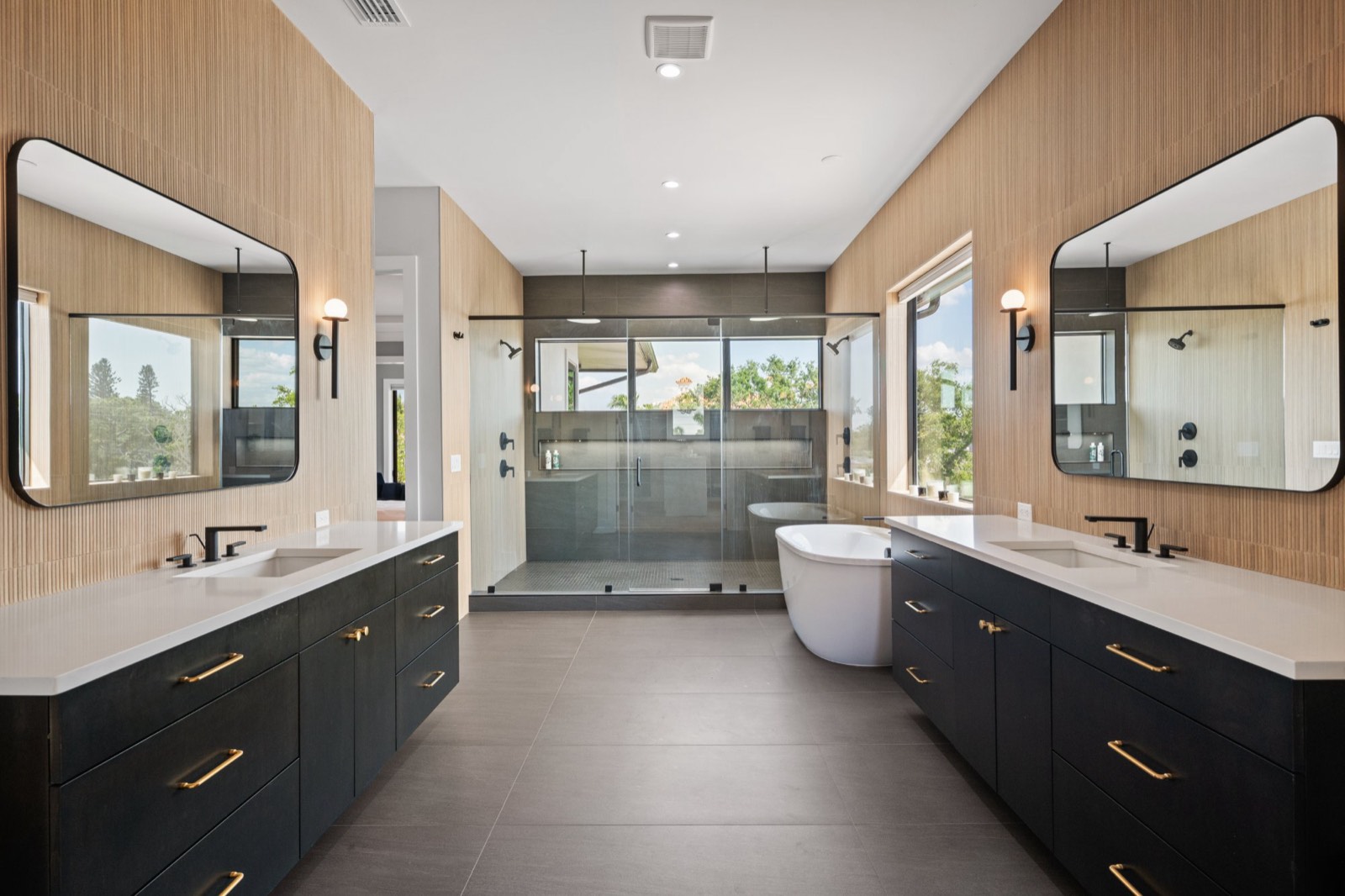 Primary bathroom with twin floating vanities, a freestanding tub and a glass walk-in shower between them
